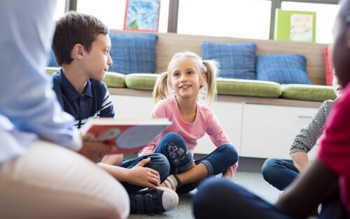 eine Gruppe Kinder sitzt im Kreis, ein Erwachsener mit Buch