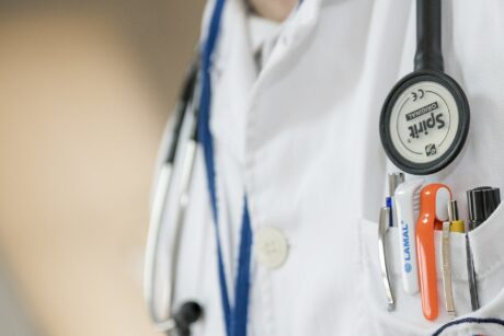 Bildausschnitt eines Arztes im weißen Mantel. Man sieht den Oberkörper mit umgehängten Stethoskop und Kugelschreiber in der Brusttasche