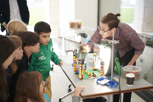 Ein junger Wissenschafter vermittelt Kindern an einem Tisch ein Experiment mit Legotürmen und Gummibärchen