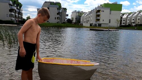 ein Bub am Flussufer mit einem Boot aus Beton