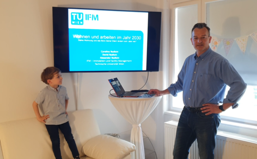 David Redlein bediehnt am Stehtisch einen Laptop und wird gleich die Präsentation am großen Bildschirm starten.