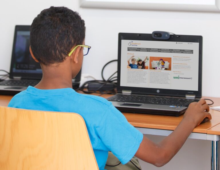 Ein Junge sitzt vor einem Laptop, auf dem die Website kinderuni.online geöffnet ist.
