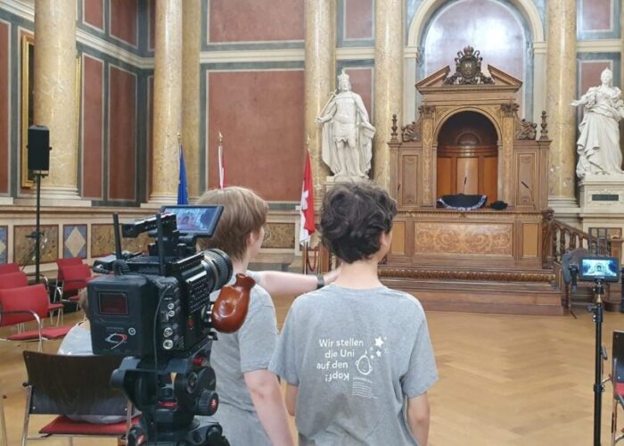 Vier kInder im KinderuniWien T-Shirt nehmen im Festsaal der Universität Wien ein Video auf