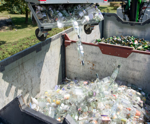 Weißgläser werden von einer ein paar Meter über dem Boden liegenden Maschine aus dem Altglascontainer in einen großen Glasbehälter hinabgeworfen