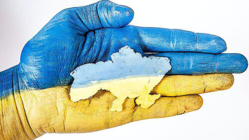 Eine Hand, angemalt in den Farben der ukrainischen Flagge, die ein Modell des ukrainisches Staates mit seinen Staatsgrenzen.