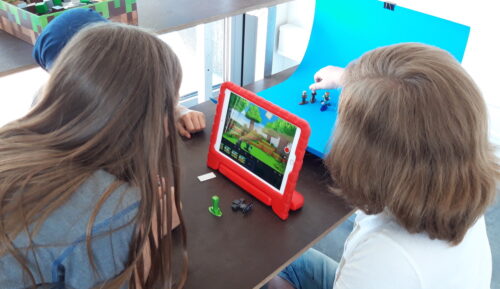 Drei Kinder machen einen Stoptrick-Film mit Tablet, Spielfiguren und Bluescreen