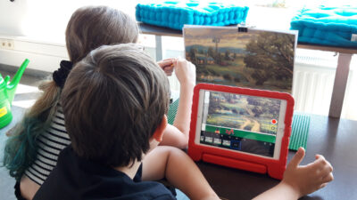 Kinder machen einen Stoptrick-Film mit Tablet, Lego-Bauplatte, Spielfiguren und einem Hintergrundbild