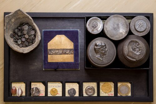 eine Sammlung verschiedener alter Zahlungsmittel, wie Muscheln und Münzen, sowie Prägestempel.
