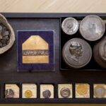 eine Sammlung verschiedener alter Zahlungsmittel, wie Muscheln und Münzen, sowie Prägestempel.