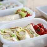 Drei Lunchboxen mit verschiedenem Inhalt. Bei der Box im Vordergrund sieht man Cocktail-Tomaten und Wraps, bei der mittleren Box ein Baguette mit Salat und in der hinteren Box Maxi.