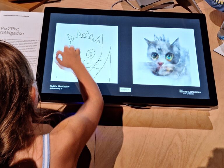 Ein Mädchen zeichnet mit den Fingern auf einem Bildschirm eine Katze.