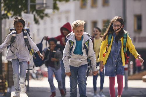 Vier Kinder, die mit Schultaschen auf dem Rücken auf deiner Straße gehen