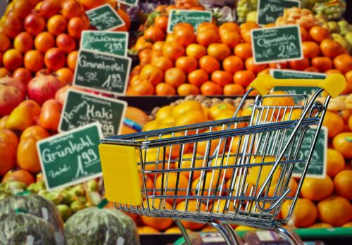 Regale mit Obst und Gemüse im Supermarkt mit einem kleinen Einkaufswagen davor