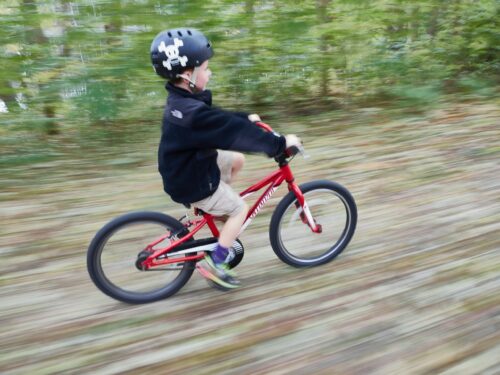 Kind mit schwarzem Piratenhelm, das auf einem roten Fahrrad dahinflitzt