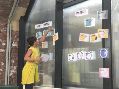 Ein Mädchen im gelben Kleid klebt einen Zettel auf eine Fensterscheibe am DOCK