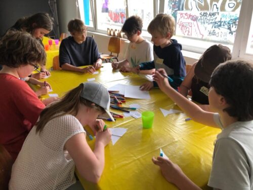 Kinder sitzen an einem Tisch und basteln Klimabotschaften