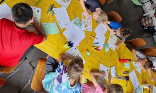 Kinder sitzen an einem langen Tisch und füllen ihren Steckbriefe aus