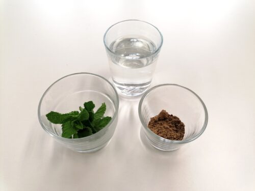 Schüssel mit frischer Minze und Schüssel mit gemahlenem Kümmel und Wasserglas