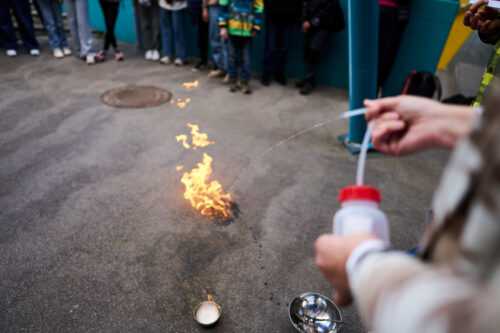Kleines Feuer auf Asphaltplatz und jemand, der mit einer Wasserflasche ausrückt