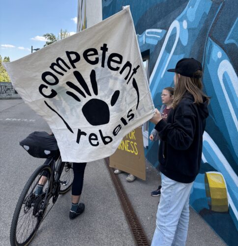 Junge Menschen stehen mit "Competent Rebel"-Flagge am Donaukanal