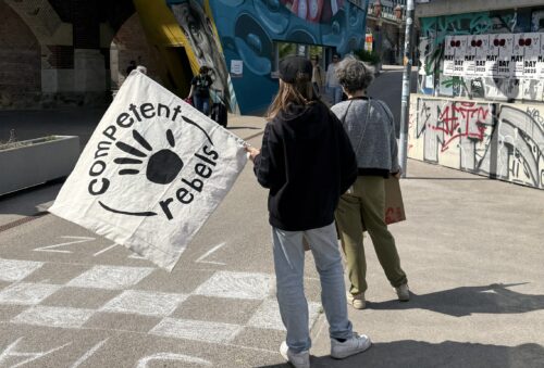 Zwei junge Menschen stehen mit der Flagge der Competent Rebels am Donaukanal und warten
