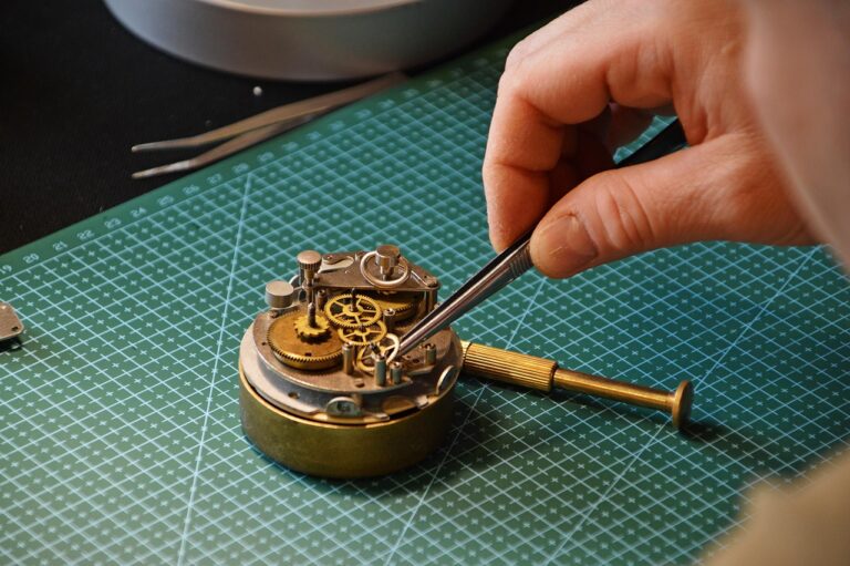 Hand, die mit einer Pinzette ein mechanisches Uhrwerk berührt