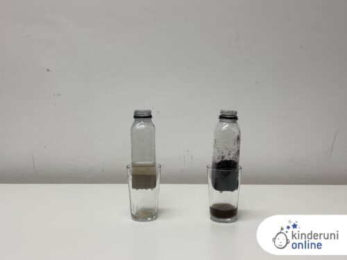 Eine Plastikflasche, die mit Erde gefüllt ist und eine, die mit Sand gefüllt ist, jeweils über einem Glas, in dem schmutziges Wasser ist.