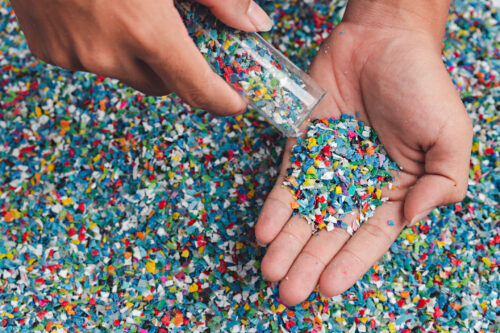 viele kleine bunte Plastikteilchen, die von einem kleinen Glas auf die Handfläche geschüttet werden