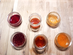 sechs kleine Gläser mit Flüssigkeiten, die unterschiedlichen rötlich-gelbe Farben haben