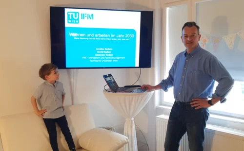 David Redlein bediehnt am Stehtisch einen Laptop und wird gleich die Präsentation am großen Bildschirm starten.
